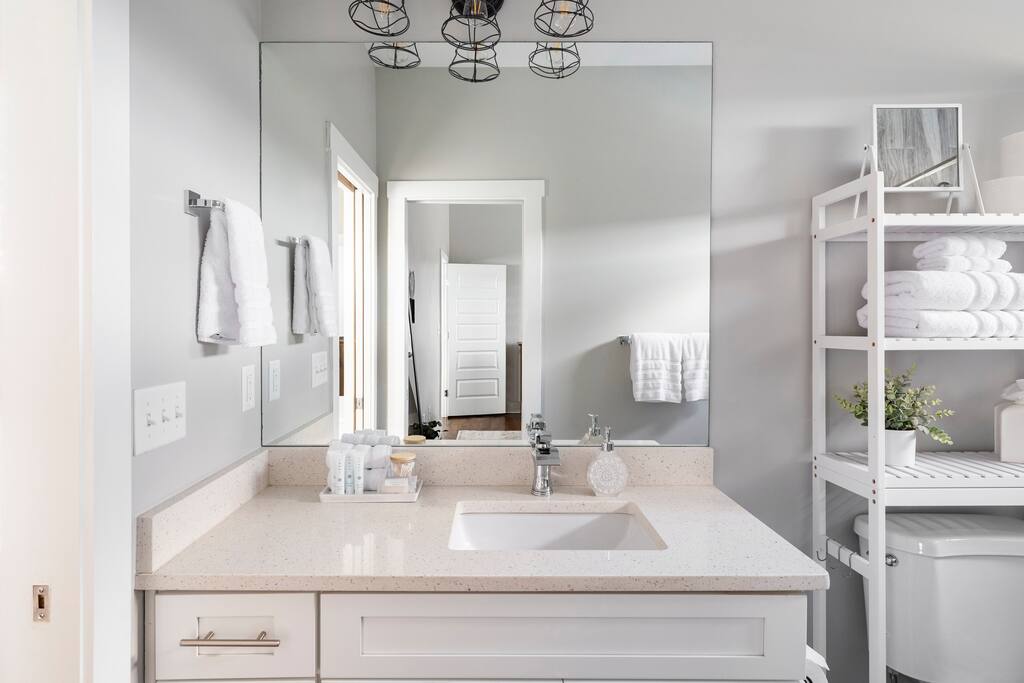 Bathroom | Jack-and-Jill | Fresh & Functional
Bright jack-and-jill bathroom with a large mirror, modern sink, open shelving stocked with towels, and thoughtful amenities—perfect for shared guest comfort.