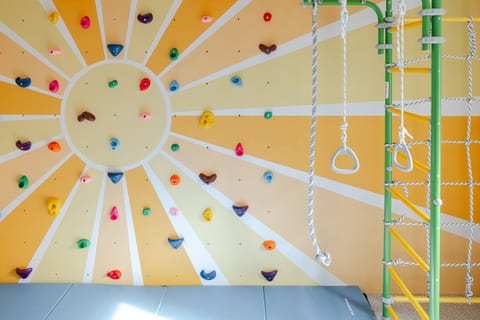 The playroom features a rock-climbing wall, rope ladder structure, stepping stones, space ship, tree house building, fort building, cash register, play kitchen, train/car table, puzzles, magnet wall, and more!