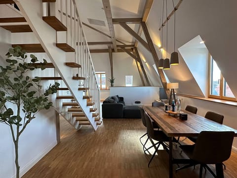 Blick aus einem der Schlafzimmer in das heimelige Loft, wo Licht und Schatten ein Spiel tanzen. Stell dir das Lachen mit Freunden am Tisch vor, die Geborgenheit auf dem Sofa.
