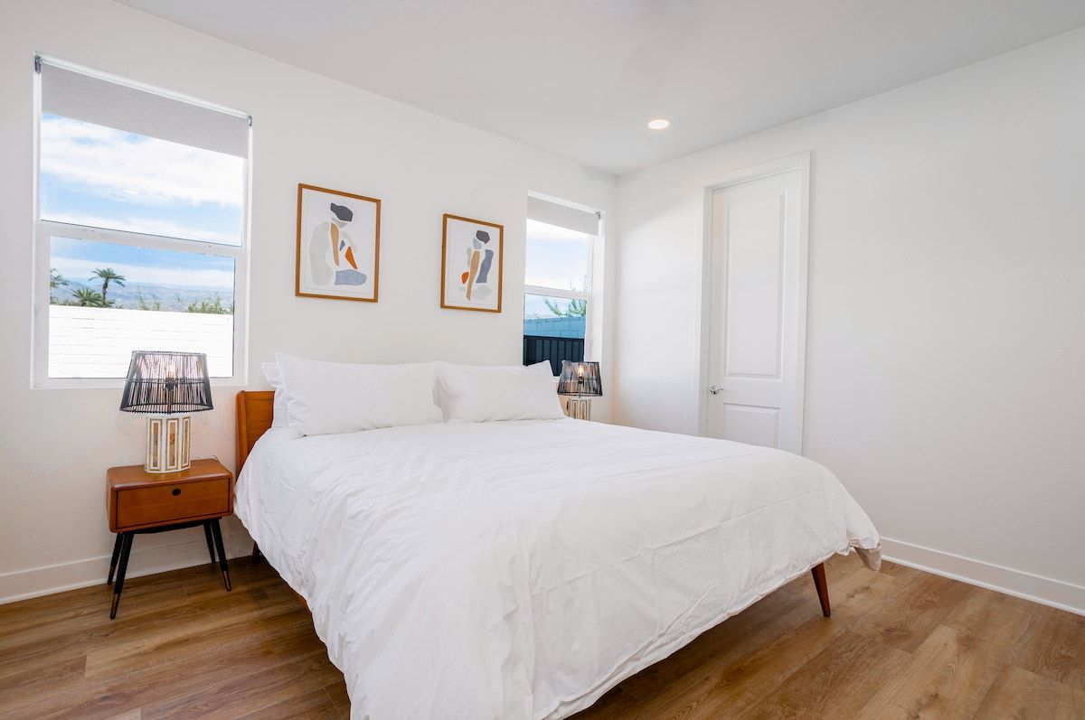 The bright first-floor bedroom emanates charm with its king-sized bed, a 55" smart TV, and a premium, comfortable mattress. Serene cream walls and soft sunlight create a cozy atmosphere.