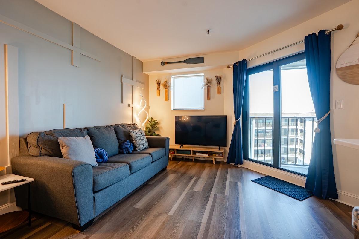 Unwind in the contemporary coastal living room overlooking the beach, where a designer wood accent wall, cozy throw pillows, modern floor lamps, a Smart TV, and a comfortable sleeper sofa come together to create a relaxing and stylish retreat.