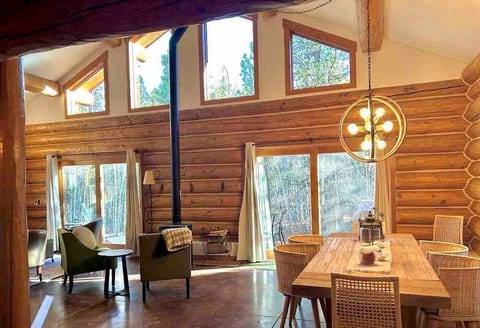 Tall ceilings of the cabin back wall showing the dining and living room areas as well as the private wooded back patio. Tall windows give visibility to the moon and start at night when possible.
