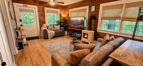 Cozy wood-paneled living room with fireplace, TV, and forest views