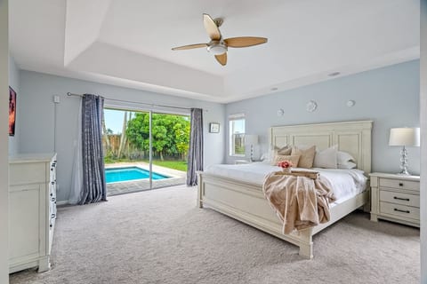 Primary Bedroom with king bed, ceiling fan, ensuite bathroom with separate tub and shower and views of the heated pool and tropical landscaping. Fort Lauderdale Area Pool Home.