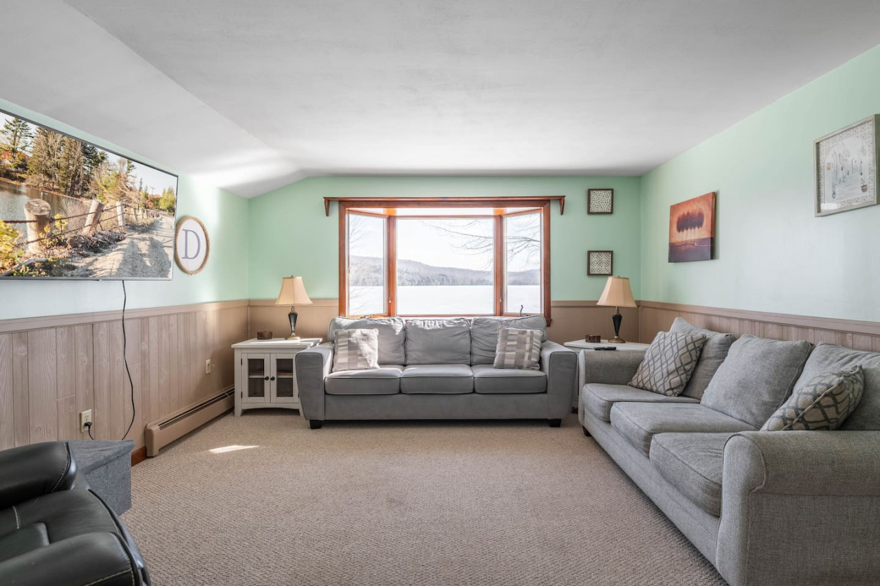 Livingroom with two couches, one of which is a sleeper sofa, recliner, and flat-screen t.v. with wifi connection - and a beautiful view of the lake from the bay window.