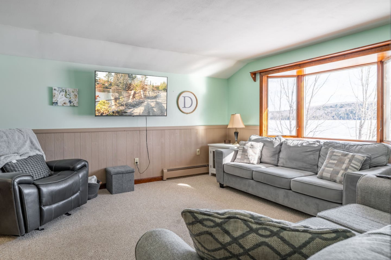 Livingroom with two couches, one of which is a sleeper sofa, recliner, and flat-screen t.v. with wifi connection - and a beautiful view of the lake from the bay window.