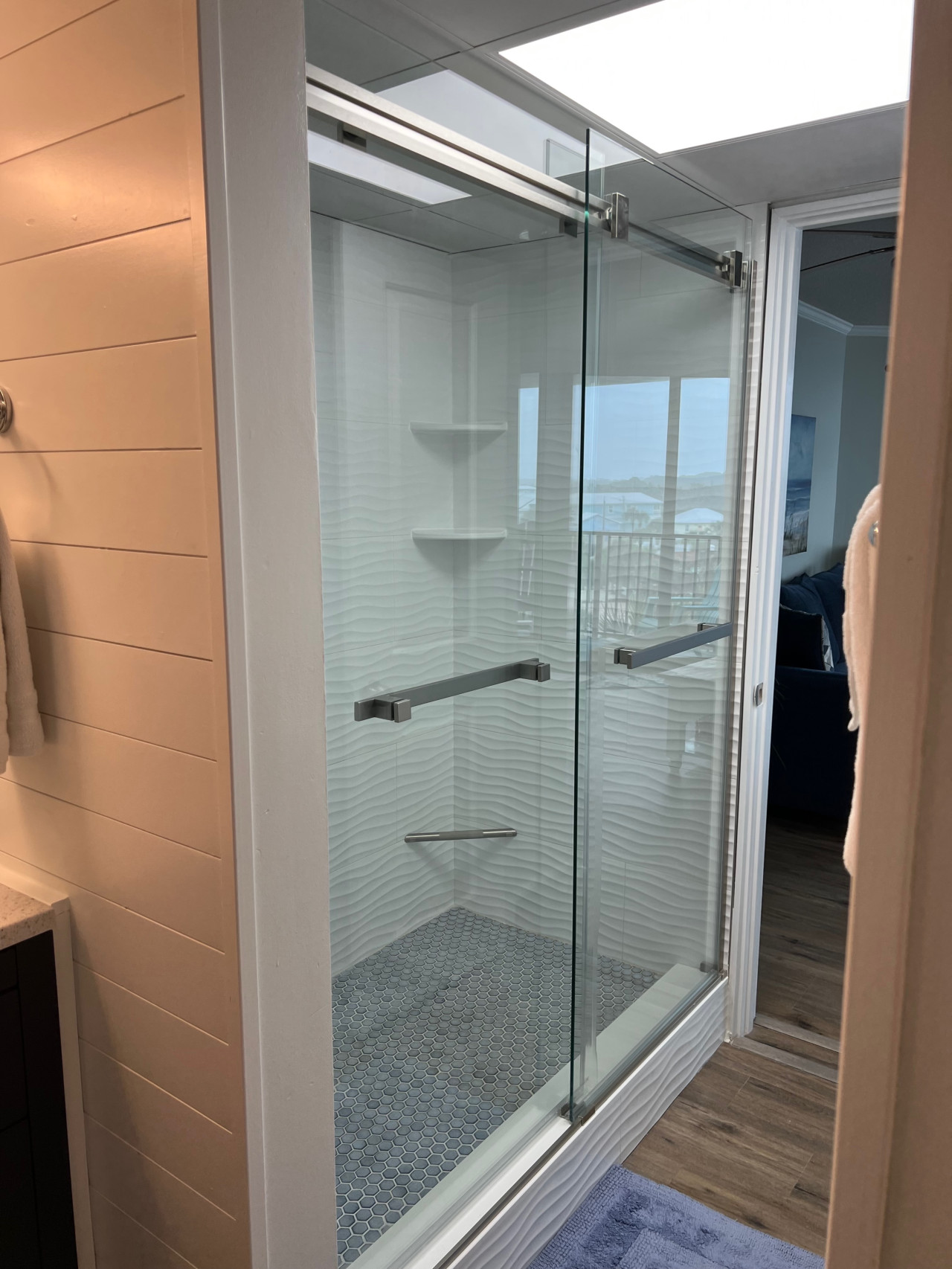Experience a modern walk-in shower with sleek glass doors, elegant wave-textured walls, and a stylish tiled floor.