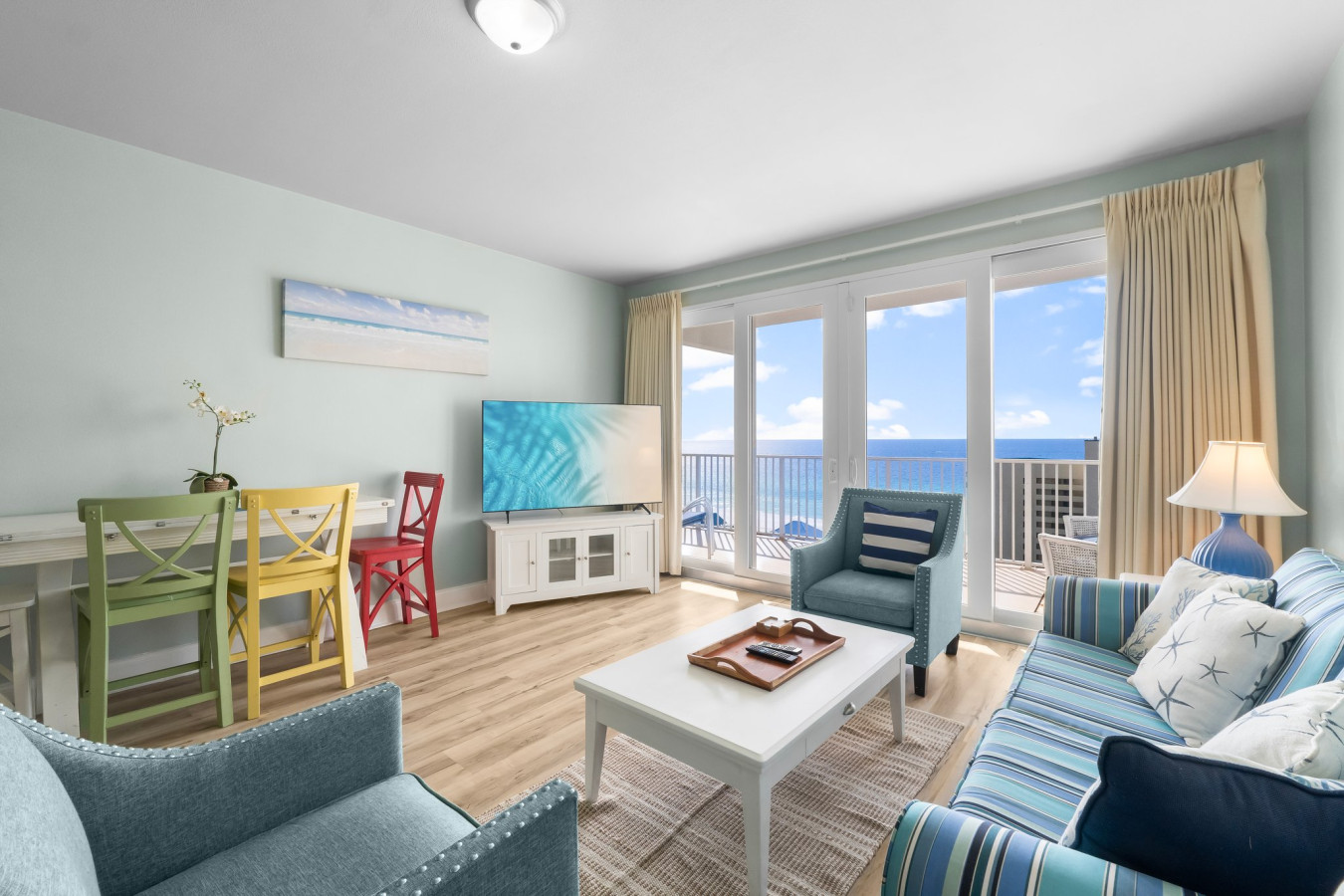 A beautifully furnished living space features vibrant seating, a flat-screen TV, and floor-to-ceiling windows opening to stunning ocean views.