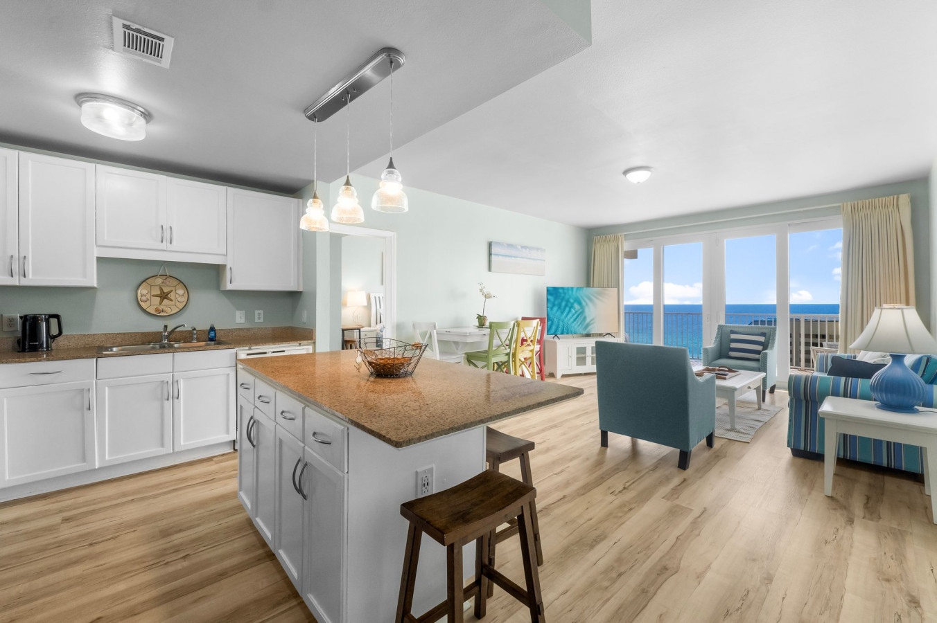 pen-concept kitchen and living area features granite countertops, a spacious island, coastal decor, and breathtaking ocean views through floor-to-ceiling windows.