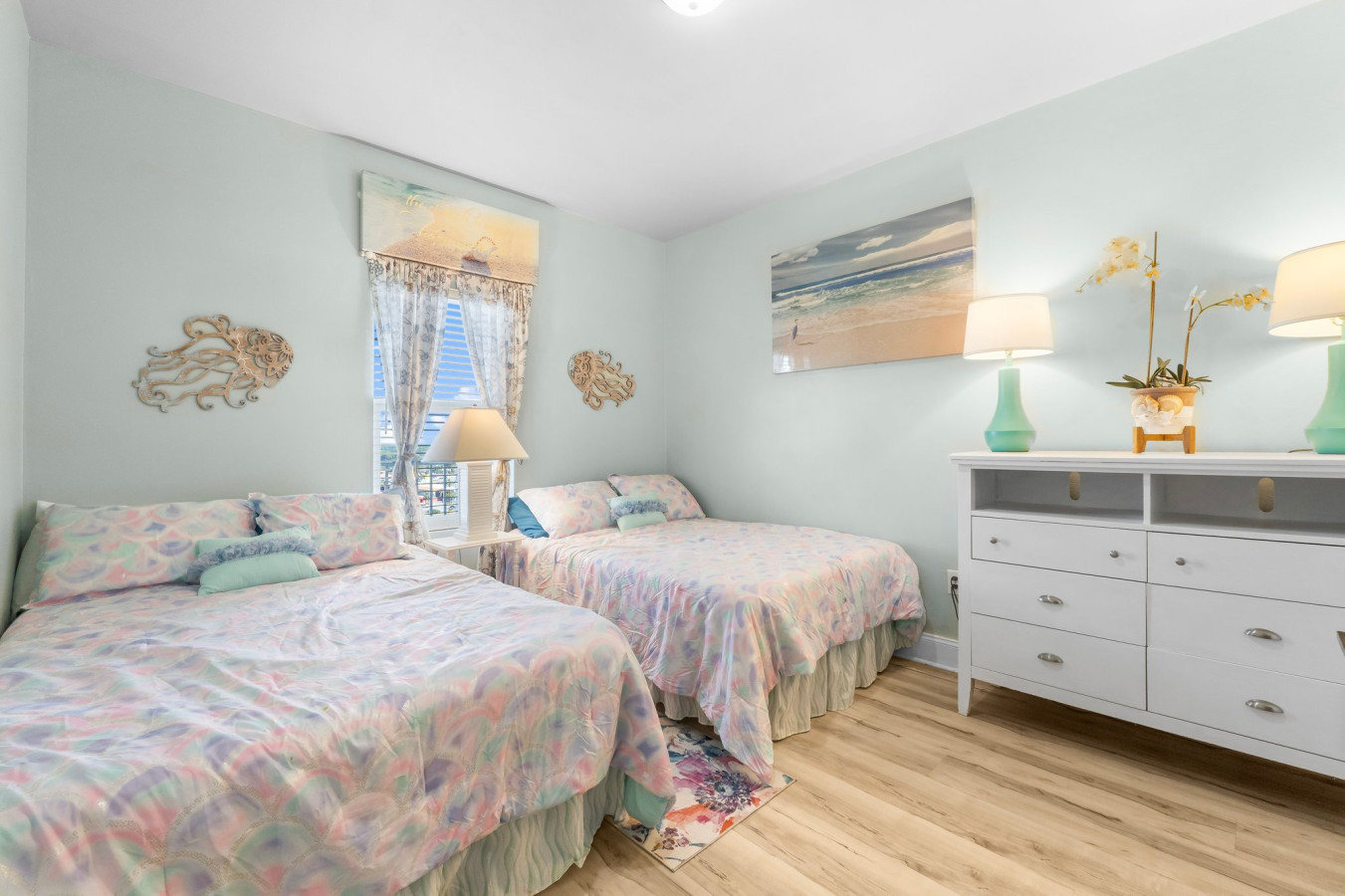 Spacious second bedroom features two full-size beds, coastal-themed decor, and soft natural lighting for a relaxing stay.