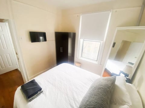 The master bedroom features a comfortable elevated Queen-size bed for luggage storage underneath. There are two nightstands, a large mirror, a spacious wardrobe, and a TV mounted on the wall.