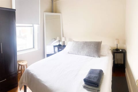 The master bedroom features a comfortable elevated Queen-size bed for luggage storage underneath. There are two nightstands, a large mirror, a spacious wardrobe, and a TV mounted on the wall.