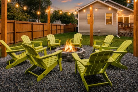Cozy fenced backyard with fire pit, string lights, and Adirondack seating