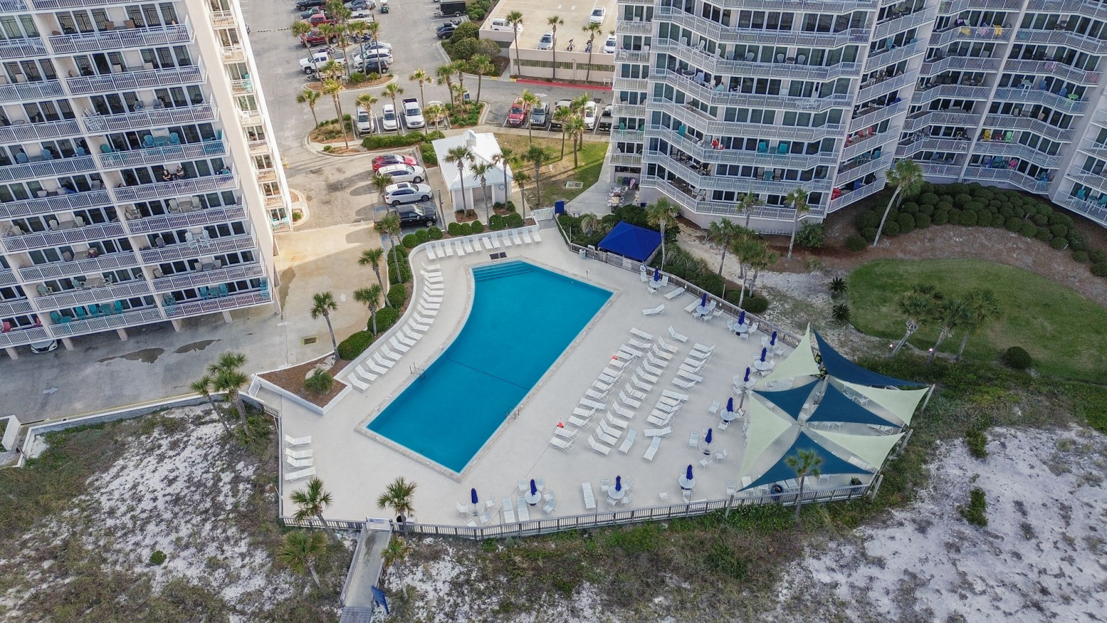 This aerial view showcases the expansive beachfront pool deck, perfectly positioned for sunbathing or enjoying ocean views just steps from the sand. With ample lounge seating and shaded areas, it's an ideal spot to unwind and soak up the coastal atmospher