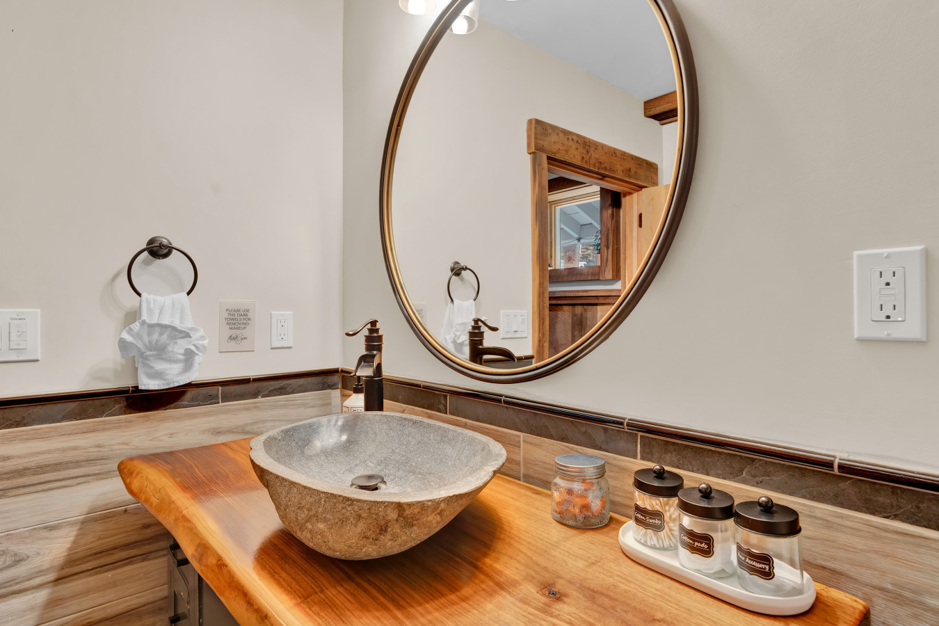 Featuring a stunning wood table, unique rock sink, and a huge round mirror — this bathroom blends rustic charm with modern elegance.