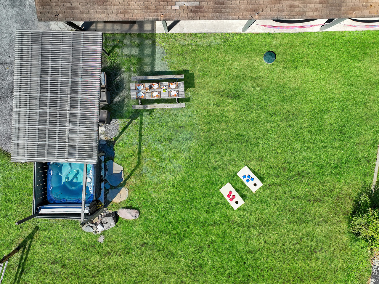 An aerial view of the backyard paradise — unwind in the hot tub, challenge friends to a game of cornhole, or enjoy a meal at the outdoor table. The perfect space for relaxation and fun!