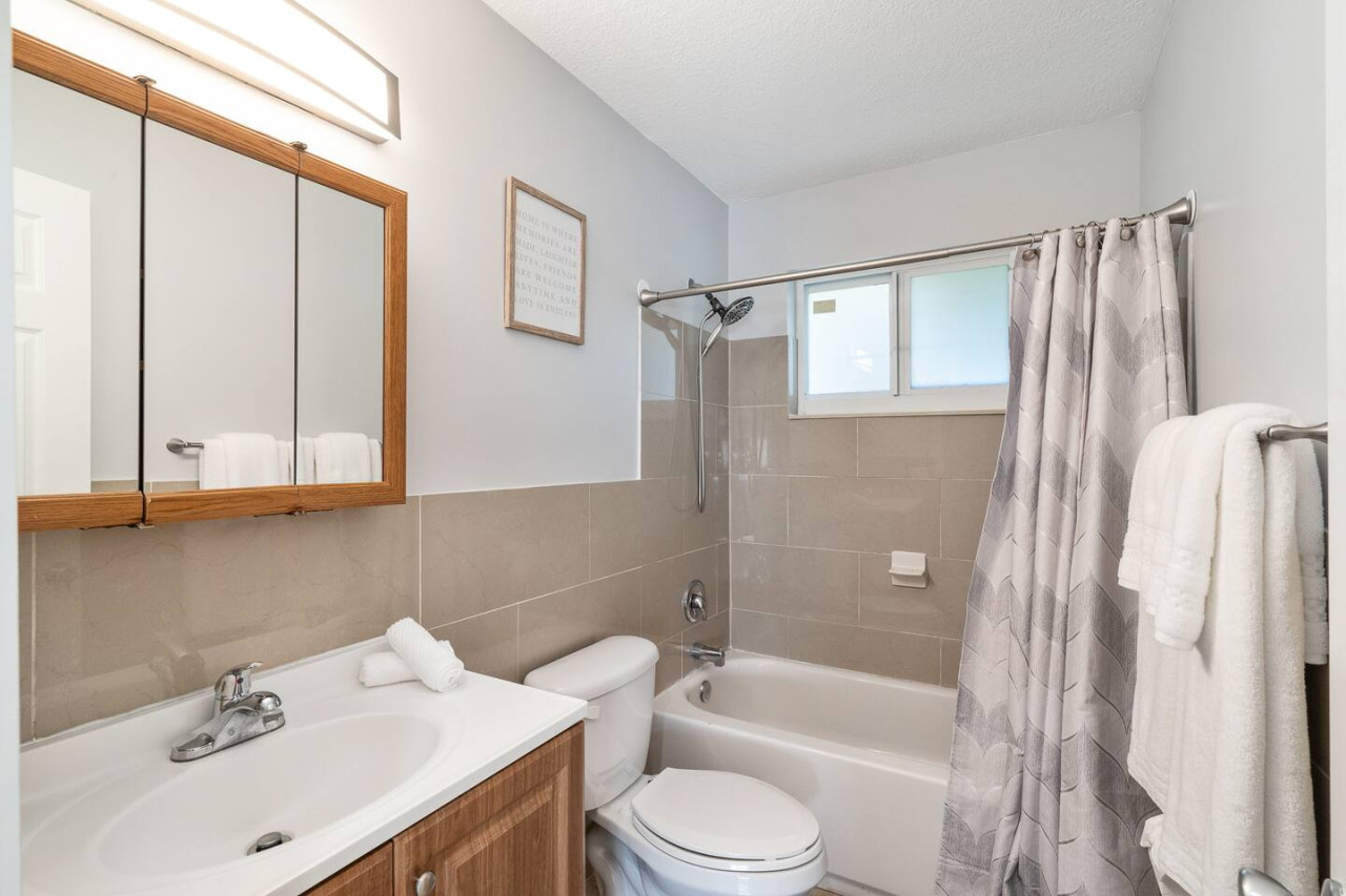 Simple and functional, this bathroom has everything you need to get ready for the day. The white walls and tile, chrome fixtures, and glass shower door create a clean and modern look. The small vanity provides storage space for toiletries, and the mirror