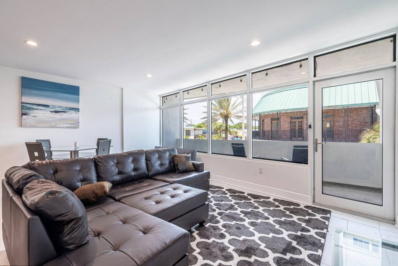 The living room is a warm and inviting space, with its comfortable couch, plush rug, and sliding glass doors that open up to a sunny patio. The geometric patterns on the couch and rug add a touch of modernity, while the plants and natural light give the r