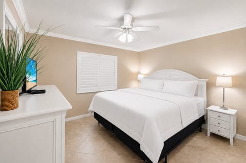 Bright king bedroom with crisp linens, TV, ceiling fan, and elegant decor