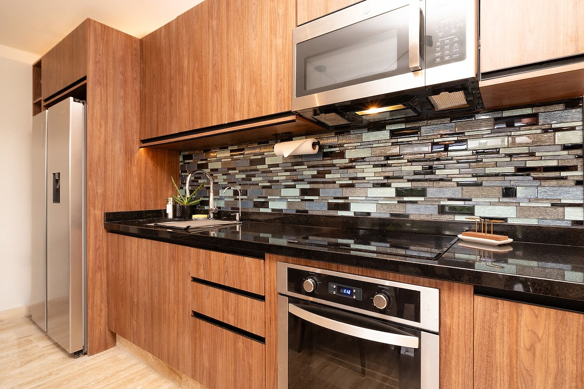 Fully equipped with sleek stainless steel appliances, including a refrigerator, oven, and microwave. The rich wooden cabinetry and stylish backsplash add a touch of elegance to your cooking experience.