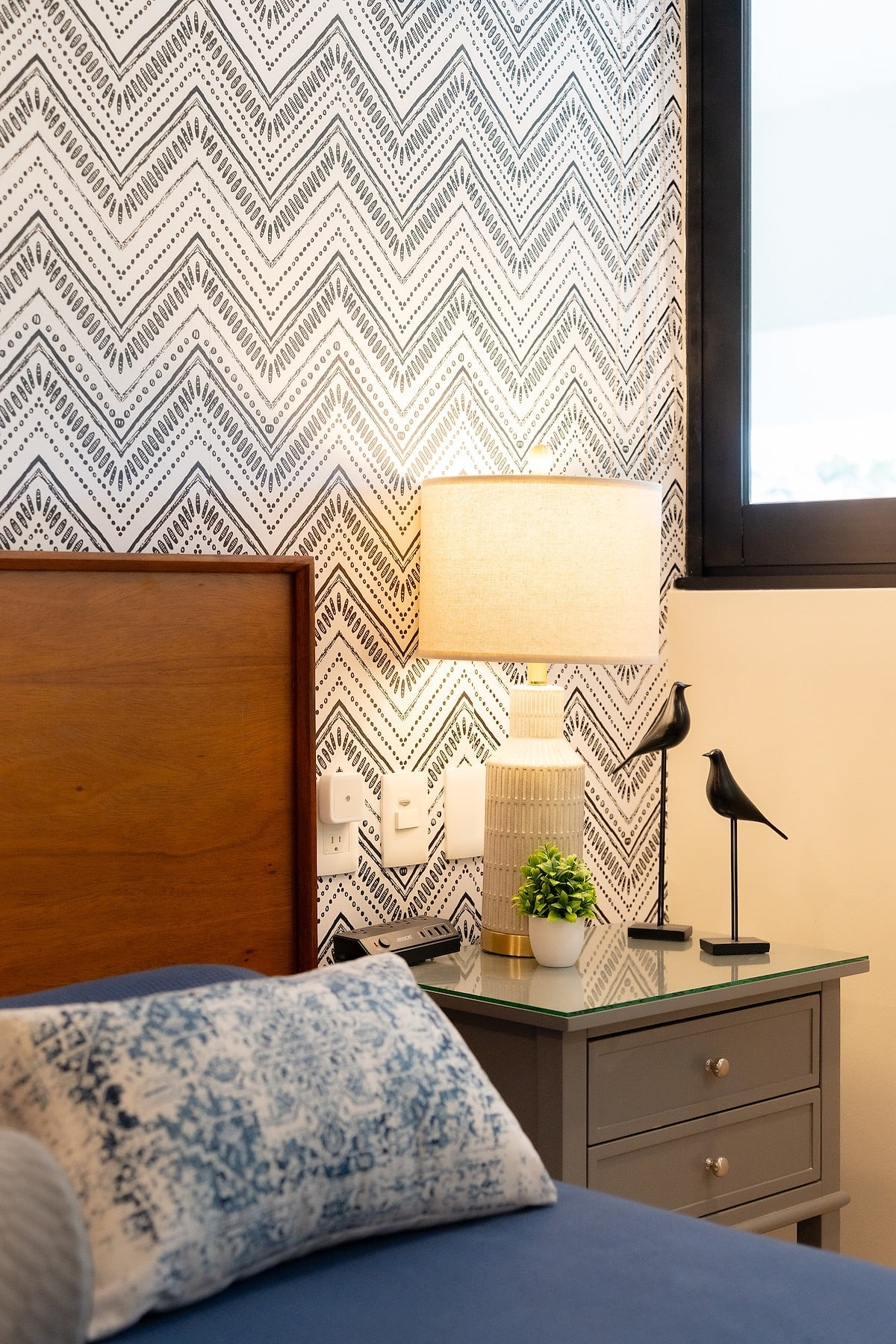 Unwind in this tranquil bedroom, featuring a comfortable bed, stylish decor, and a touch of bohemian charm. The patterned wallpaper and soft lighting create a peaceful ambiance, perfect for a restful night's sleep
