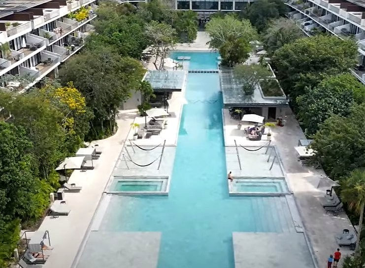 Expansive resort-style pool at AWA Playacar, surrounded by lush jungle landscaping in Playa del Carmen, Mexico