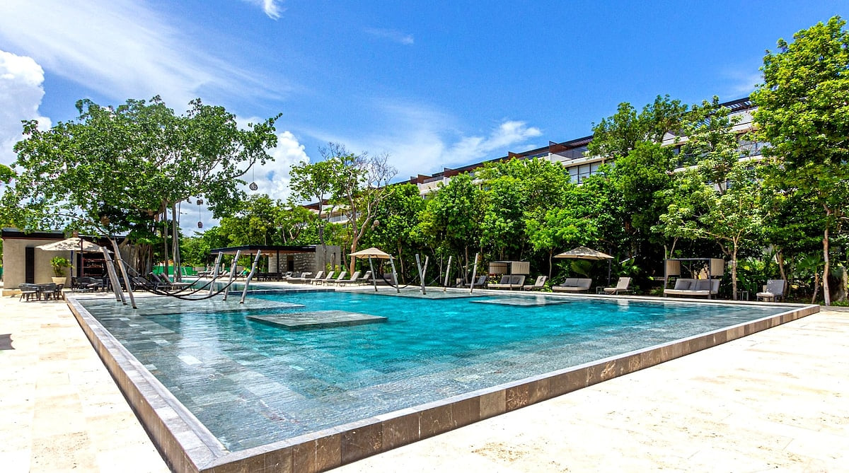 Spacious resort pool with shaded loungers and tropical greenery at AWA Playacar in Playa del Carmen
