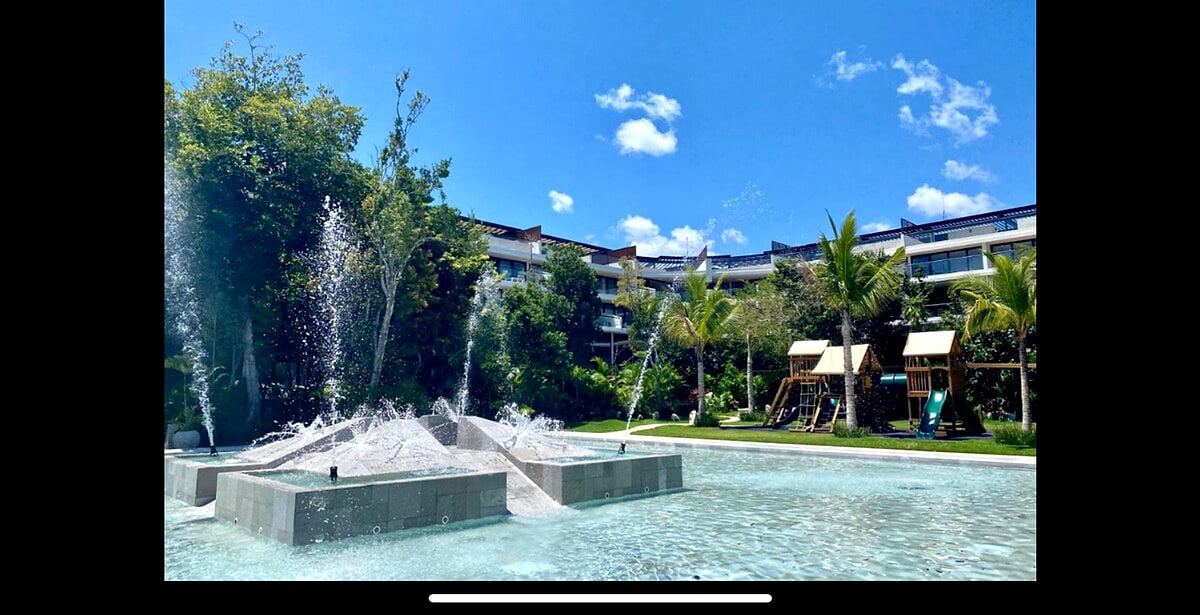 Kids splash pool with playful water fountains, surrounded by tropical gardens and family-friendly amenities at AWA Playacar