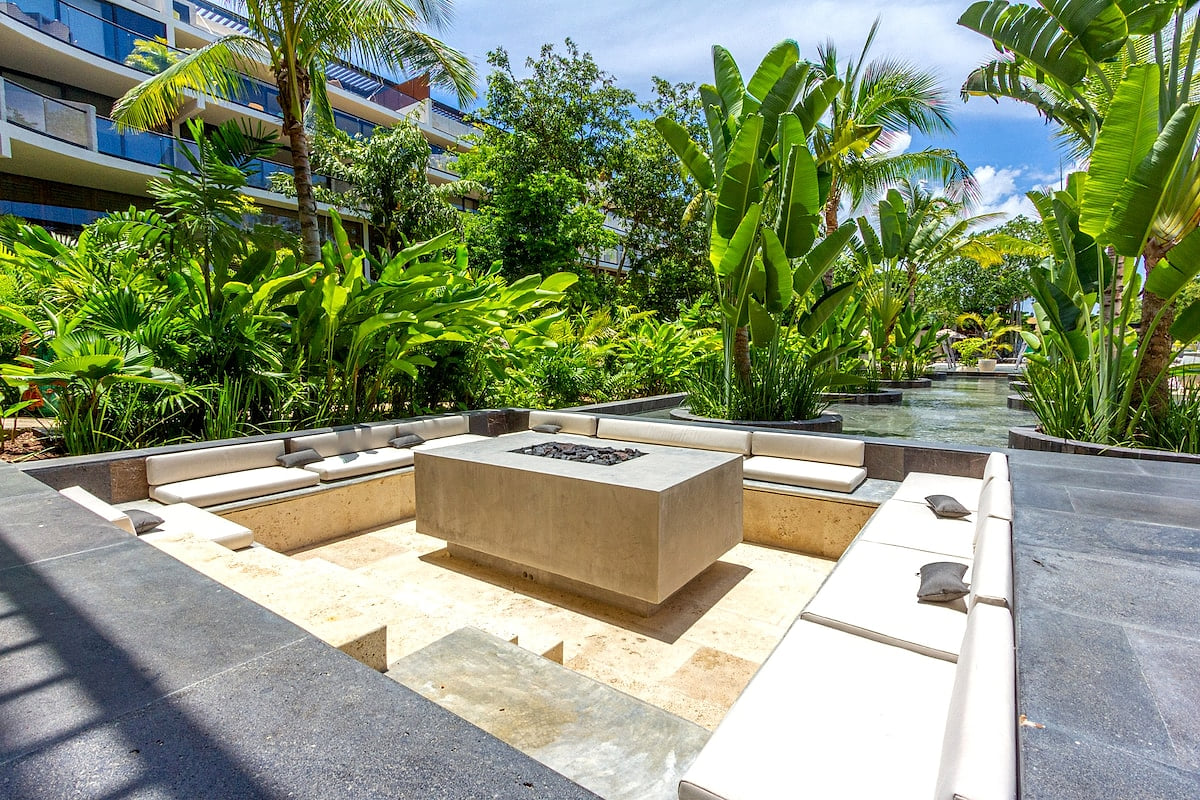Outdoor fire-pit lounge surrounded by tropical landscaping at AWA Playacar, a relaxing shared space for guests to unwind during their Playacar vacation
