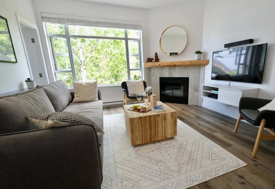 Living Room - The fireplace is tucked in the corner for those cooler nights.  The big window faces east for the morning sun and has a view of the forest and peaks of Blackcomb mountain.Note: Wine & food is staged for illustration (not included)