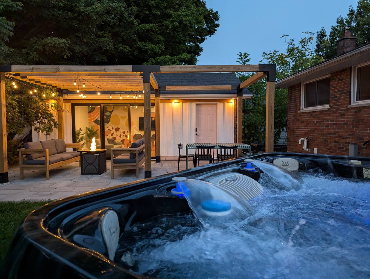 Brand new hot tub as of summer 2024. Patio with ample lounge seating, propane fire table and dining table. Games room in the background.