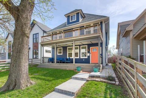 Charming two-story home with a navy-blue exterior, white trim, and a vibrant orange front door. It features a spacious front porch with seating, a balcony on the second floor, and a well-maintained front yard with a concrete walkway