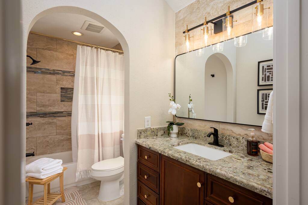 A sophisticated bathroom featuring a relaxing bathtub, essential towels, a contemporary toilet, a sleek sink, and a large mirror for added style.