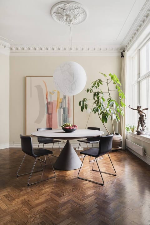 Dining area with a eye catching design table, black chairs, and extra stools for larger gatherings. Tall windows provide natural light, complemented by abstract art on the wall, from the owners gallery collection.