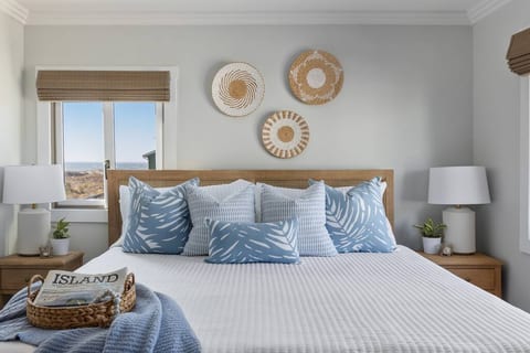 Upstairs bedroom with a comfortable king bed, stylish coastal decor and stunning views of the ocean and pool