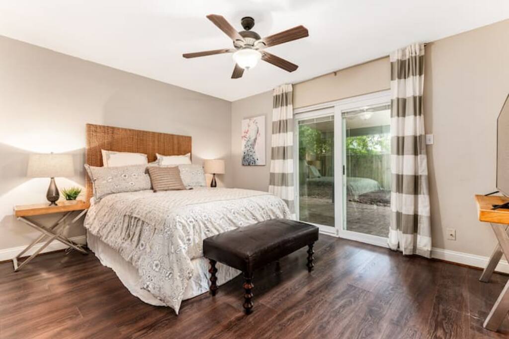 This inviting bedroom combines a window view, ceiling fan, Tv and side lamps with soft, complete bedding