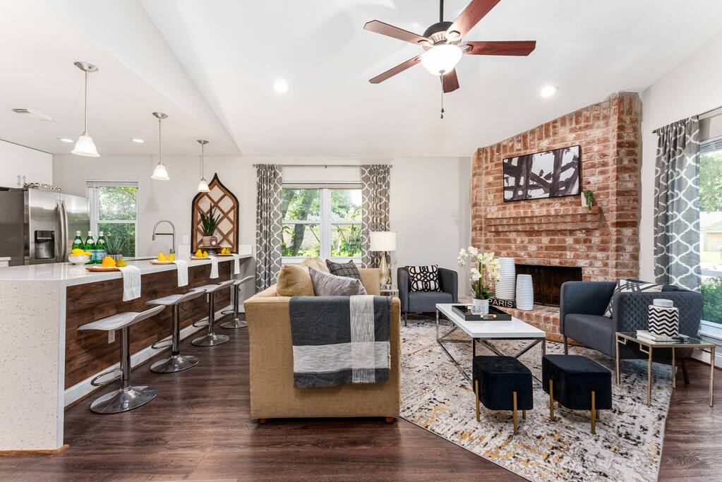 A welcoming living room with a sofa, open-concept kitchen, large window, and ceiling fan, creating a comfortable and relaxing space for all