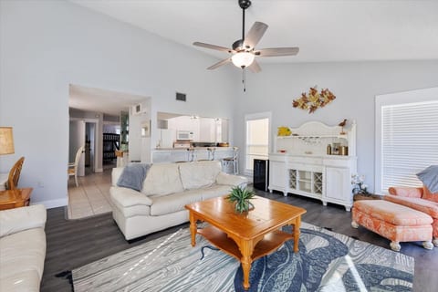An alternate angle of the living room highlights the open-concept design, with a view of the dining area and the kitchen beyond. The room is tastefully decorated with coastal-themed accents and plenty of natural light from multiple windows.