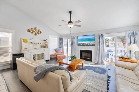 The living room is bright and inviting, featuring a cozy seating area with two comfortable leather couches and a matching armchair. A flat-screen TV is mounted above the fireplace, and large sliding glass doors open to a spacious balcony.