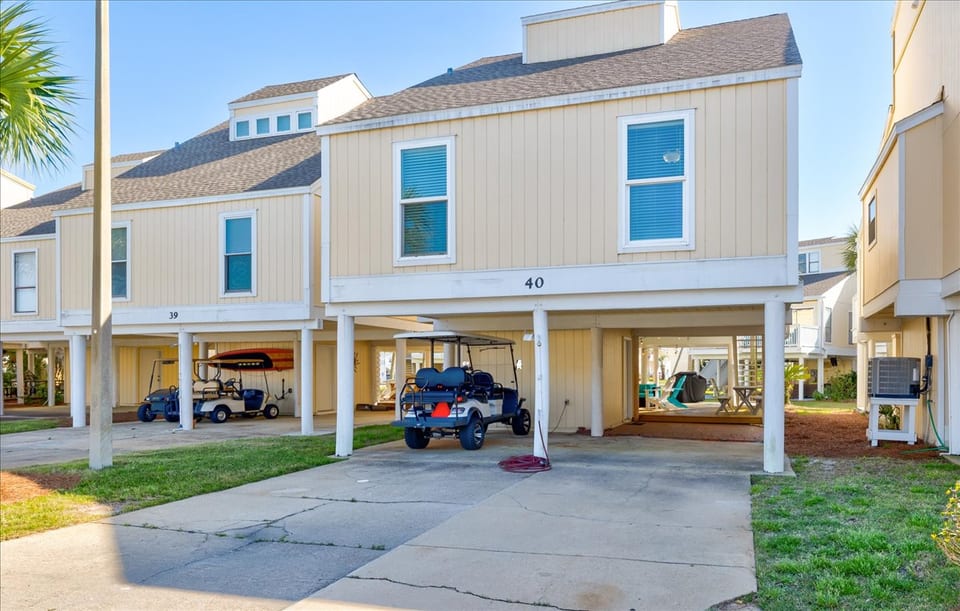 A front view of the property, showcasing its charming coastal design with elevated parking underneath. The designated parking area includes space for vehicles, golf carts, and boat trailers (up to 30 feet long).