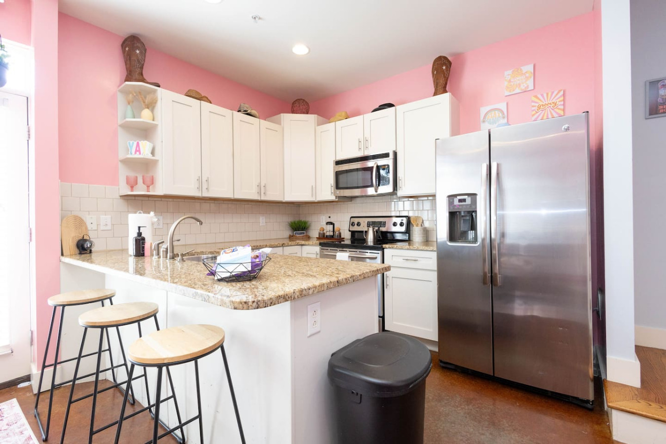 A fully stocked kitchen with stainless steel appliances and plenty of counter space for group meals or morning mimosas. The white cabinets pop against the playful pink walls, making even breakfast feel Instagram-worthy.
