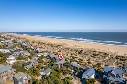 Sweeping coastal view over sandy shores, rooftops & endless ocean horizons.