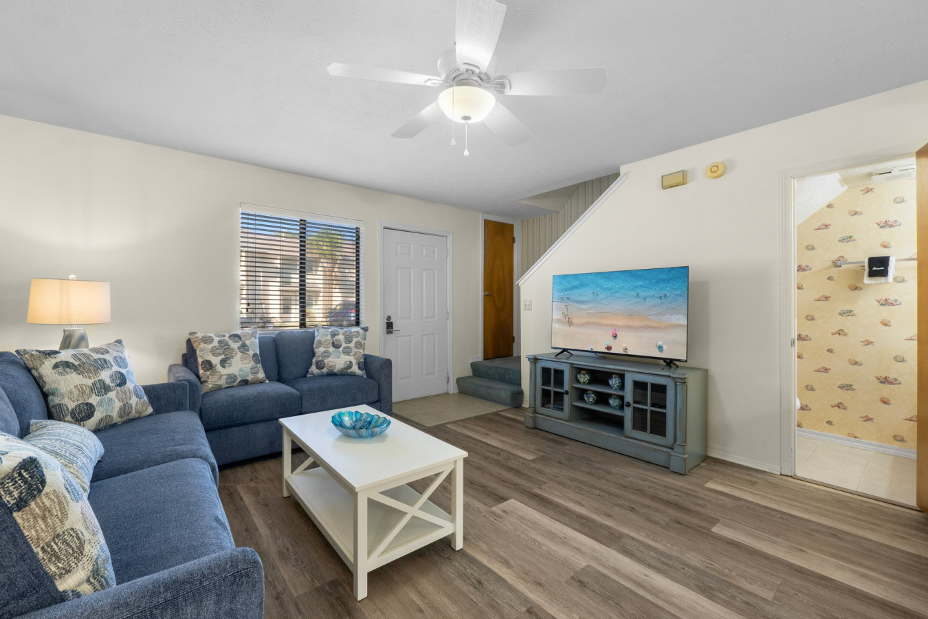 Living Room: Bright and inviting living space with a queen-size sleeper sofa, beach-inspired décor, and a large smart TV — perfect for relaxing after a day in the sun.