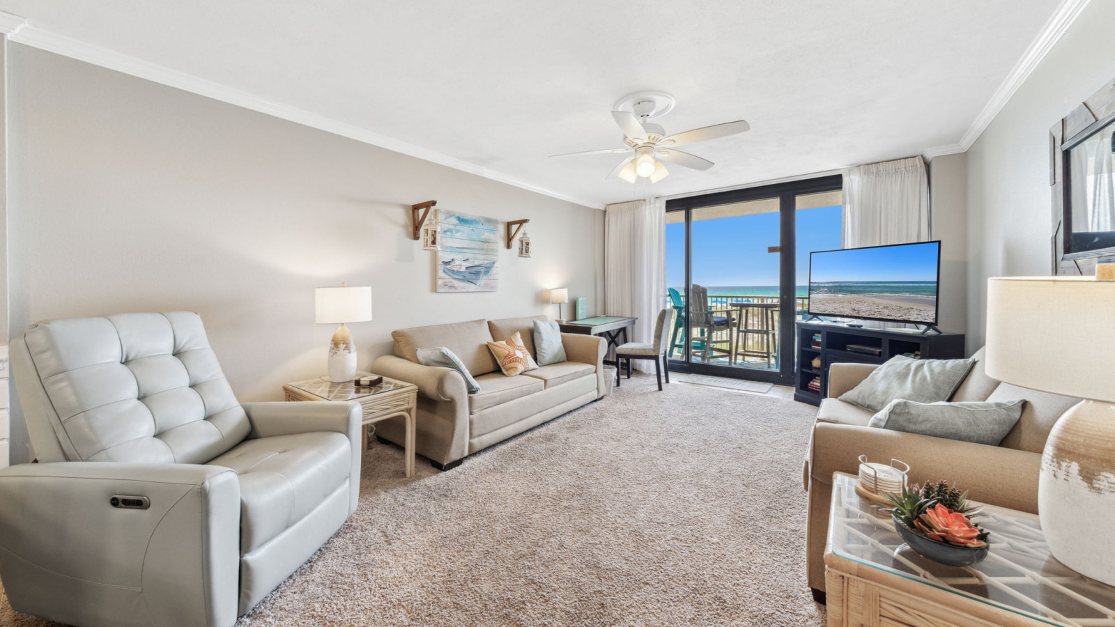 This cozy living room features plush seating, coastal décor, a large TV, and sliding doors to a private Gulf-front balcony.