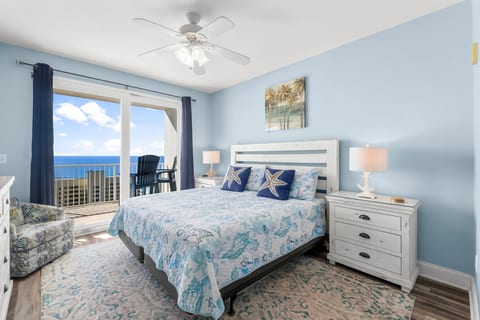 spacious master bedroom features a king-sized bed, coastal decor, and direct balcony access with serene ocean views