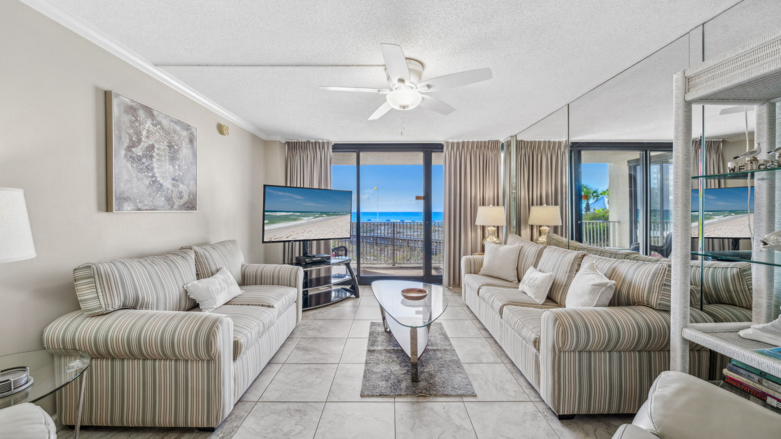 Relax in a bright living room with striped sofas, a glass coffee table, Gulf views, and balcony access.