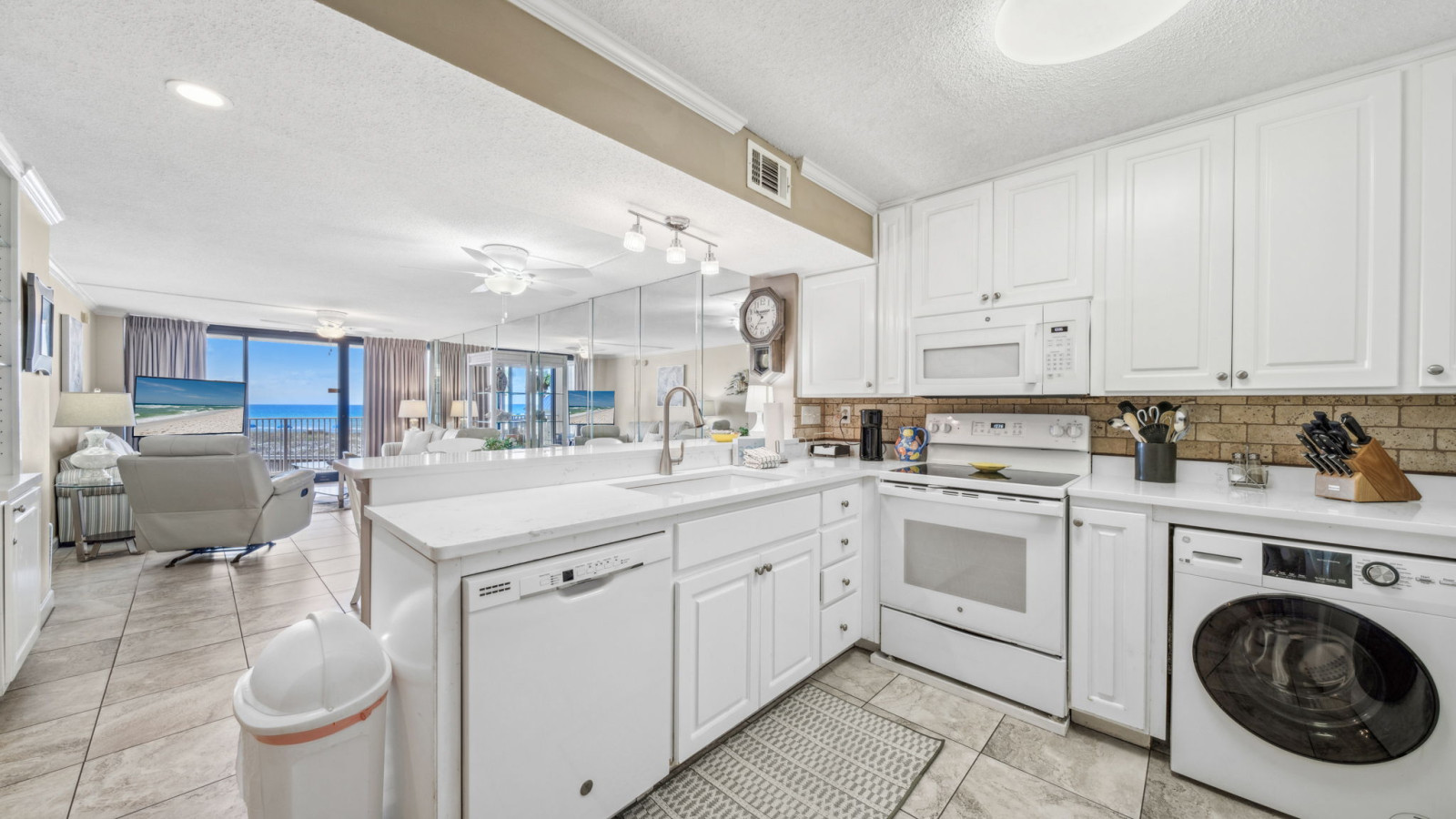 Cook easily in this bright kitchen with white cabinets, full-size appliances, in-unit washer/dryer, and Gulf views through the open layout.