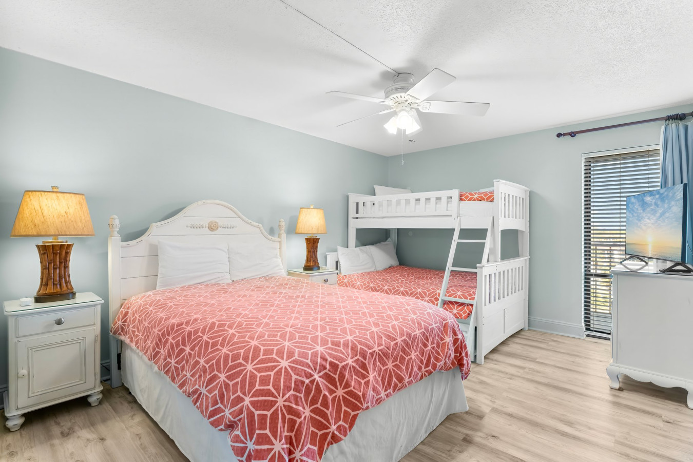 This charming bedroom features a full-size bed, a twin-over-full bunk bed, coastal-inspired decor, and a cozy ambiance perfect for families or groups seeking a comfortable and stylish retreat.