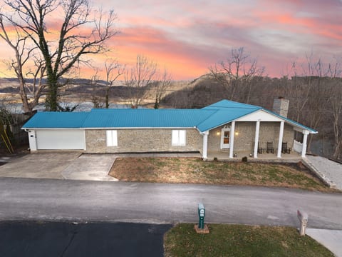 Stone lakeside ranch with blue roof, garage, and relaxing front porch.