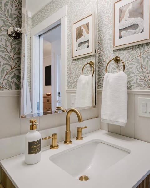 Elegant bath vanity with brass fixtures and charming botanical wallpaper